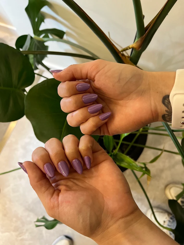 Unhas amendoadas em lilás com plantas ao fundo